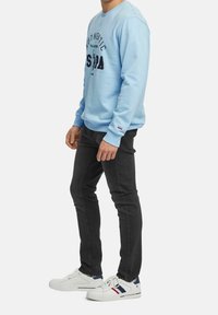 Ljusblå sweatshirt med grafisk text, rund hals, ribbade ärmslut; matchad med svarta jeans och vita sneakers med marinblå detaljer.