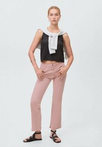 Svart kort topp, rosa högmidjade jeans med franskant, grå tröja drapera över axlarna, och svarta remsandaler.