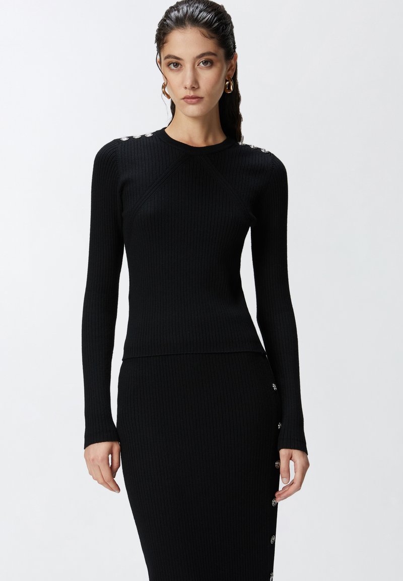 Maglione nero a coste con maniche lunghe, caratterizzato da dettagli sulle spalle con bottoni argentati e un design aderente.