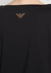 Czarny bawełniany t-shirt z szerokim dekoltem i subtelnym logo z złotych kryształków na plecach, dodający faktury i detali.