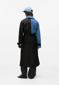 Czarny i niebieski trencz w stylu color-block, wykonany z połączenia denimu i materiału, z paskiem w talii, długimi rękawami i niebieską czapką. Gładka tekstura i dopasowany krój.