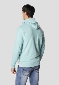 Jasnoniebieska bluza z kapturem wykonana z bawełnianej mieszanki, z kieszenią kangurka i ściągaczami na rękawach, w zestawie z wyblakłymi niebieskimi dżinsami.