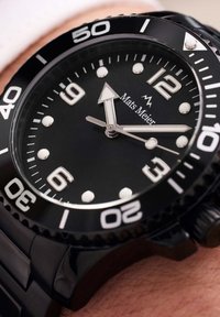 Montre de plongée noire avec un cadran rond, marqueurs horaires blancs et aiguilles luminescentes. Équipée d'une lunette noire et d'un bracelet en acier inoxydable. Nom de la marque visible.