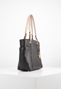 Svart läder tote-väska i pebble-textur med ljusbeige läderhandtag och detaljer i guldton. Har en strukturerad form och sidofickor.