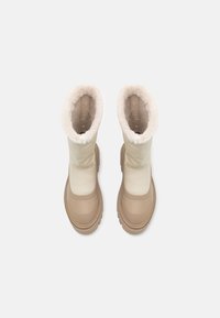 Pari talvi-saappaita vaaleanbeigeinä, joissa on paksut kumipohjat ja kermaisen värinen tekoturkislaitteisto, nähtynä ylhäältä valkoista taustaa vasten.