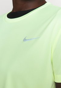 Zbliżenie na osobę noszącą jasnoszary t-shirt Nike z małym, odbijającym światło, srebrnym logo Nike na klatce piersiowej.