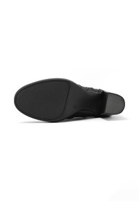 Suola di una scarpa elegante nera con tacco testurizzato e suola anteriore liscia su uno sfondo bianco.