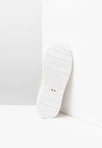 Suola di sneaker bianca con gomma testurizzata per una migliore aderenza, forma arrotondata e un piccolo dettaglio della bandiera italiana vicino all'etichetta della taglia.