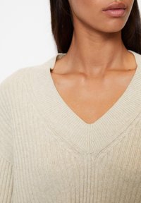 Maglione beige a scollatura a V con texture a coste e dettagli a treccia lungo il colletto, caratterizzato da una vestibilità morbida e un tessuto morbido.