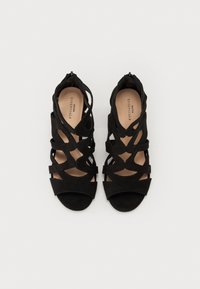 Zwarte suede high-heeled sandalen met uitsnijdingen, open tenen en een soepele binnenvoering. Ritssluiting aan de achterkant.