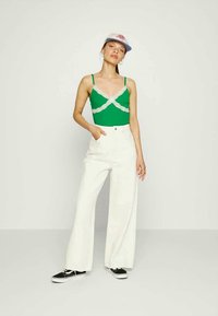 Top verde com renda na bainha, combinado com calças largas brancas e ténis pretos. Inclui um boné de basebol com um logotipo vermelho.