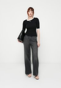 Svart kortermet topp med hvit kragedetalj, sammen med vide mørke jeans. Modellen holder en skinnende svart håndveske. Glatte teksturer gjennom hele antrekket.