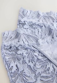 Țesătură din dantelă albastru deschis cu modele florale și margini ondulate, suprapuse pe un material neted asortat.