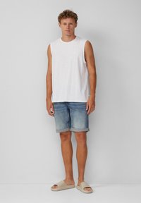Chemise sans manches blanche, shorts en denim bleu avec ourlets retroussés, sandales à glisser beiges ; tenue d'été simple et décontractée.