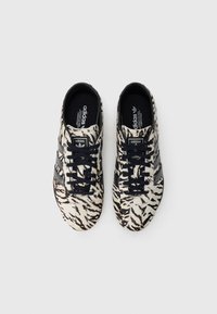 Αθλητικά παπούτσια με φάσεις ζέβρας σε ασπρόμαυρο, με μαύρα κορδόνια και τρεις μαύρες ρίγες στα πλάγια. Λεία υφή και στρογγυλεμένη σχεδίαση στη μύτη.