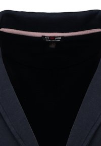 Primo piano di un colletto di felpa nera e blu scuro con un orlo interno rosa e un piccolo etichetta nera con la scritta "Key Largo fondato nel 1990."