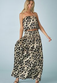 Zwart en beige strapless crop top en bijpassende maxi rok met een gevlekt patroon. De stof is soepel met een geraffineerde tailleband en een vloeiende uitstraling.