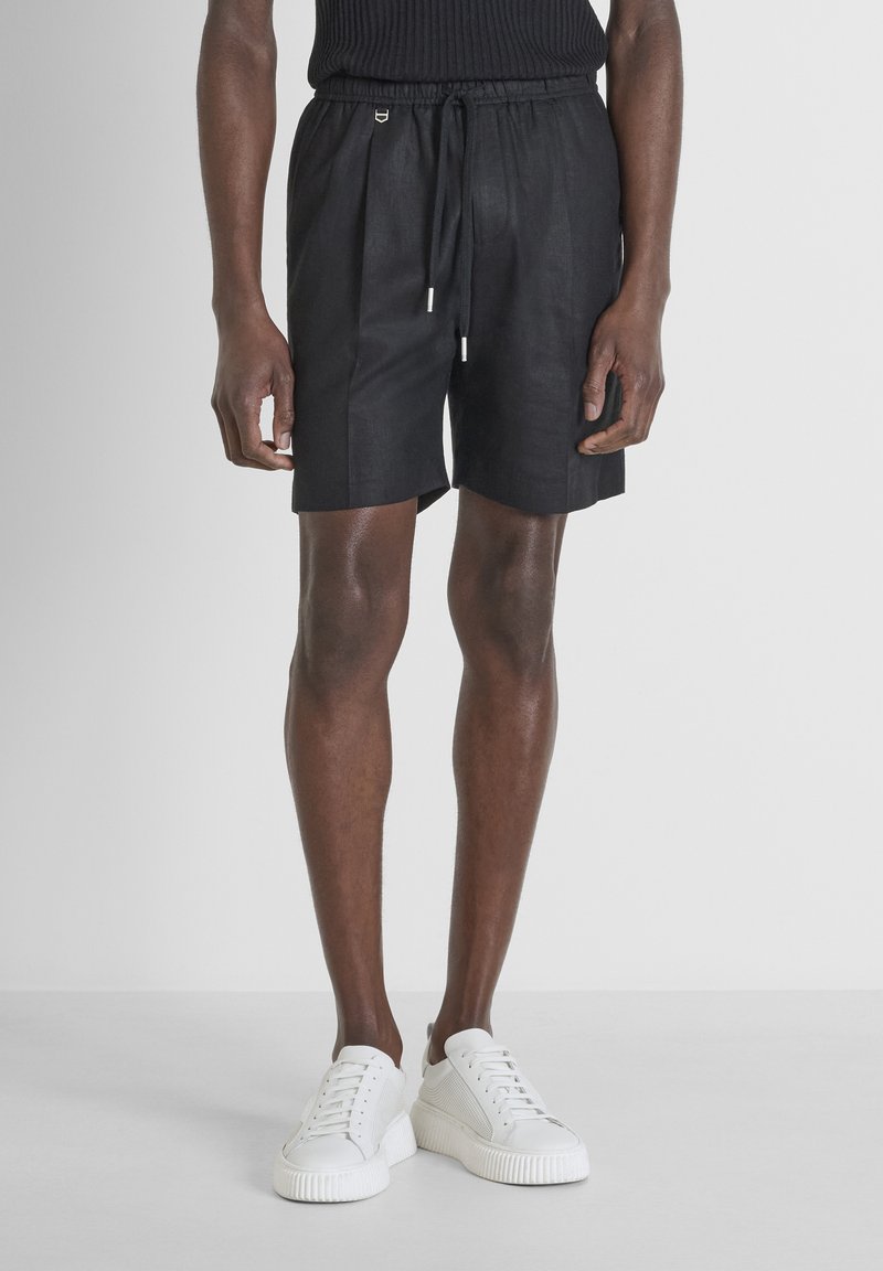 Shorts neri in lino con vita elasticizzata e cordoncino, caratterizzati da una vestibilità rilassata. Abbinati a sneakers bianche.