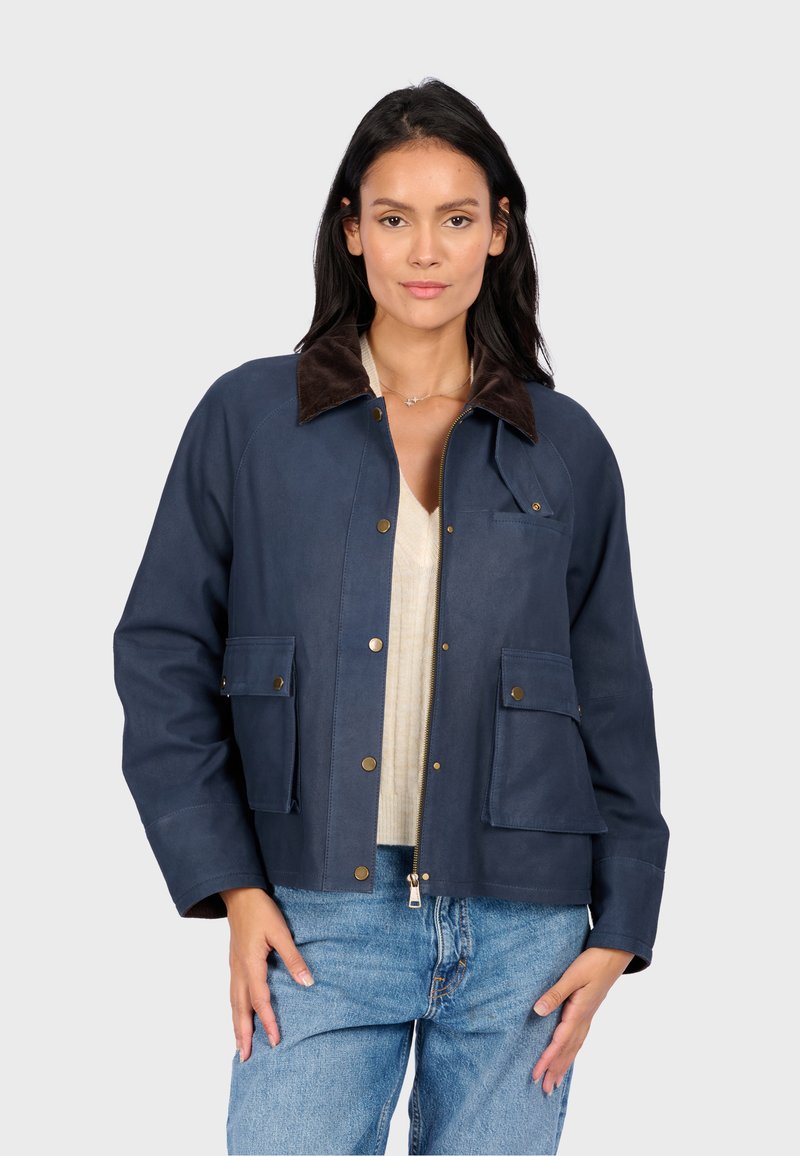 Námořnická modrá nepropustná bunda s hnědým semišovým límcem, předním zipem a kapsami na patentky. Má volný střih a raglánové rukávy.