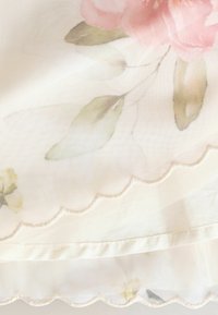 Durchscheinender Stoff mit floralem Muster in Rosa und Grün, mit gewellten Kanten und einer weichen Textur, die Leichtigkeit und Zartheit verstärken.