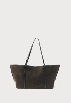 Sac cabas rectangulaire en daim brun foncé avec de longues poignées en cuir noir et un design minimaliste sur un fond uni.