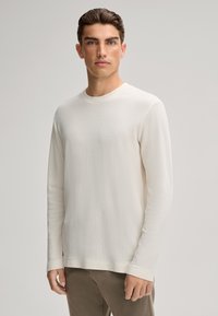 Helles Creme langärmliges Shirt mit Rundhalsausschnitt und strukturiertem Strick. Glattes Material, lockere Passform und dezente Nahtdetails.