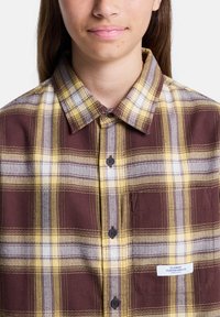 Brun, gul och vit rutig skjorta med knappar, klassisk krage, texturerad tyg, bröstficka och en liten logotags.