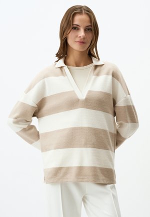 Pull en beige et blanc rayé à col V, fabriqué en tissu doux. Présente une coupe décontractée et des fentes latérales à l'ourlet.