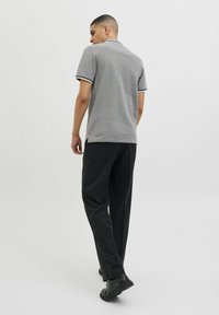 Grijze polo met contrasterende gestreepte kraag, gecombineerd met zwarte broek en zwarte schoenen. Model wordt van achteren bekeken.
