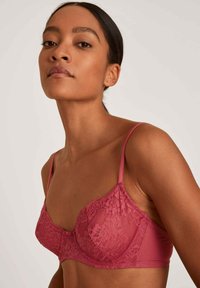 Kanten beha in zacht roos, met verstelbare bandjes en een bloemenpatroon. Glad materiaal met beugelondersteuning en een decoratieve strik in het midden.