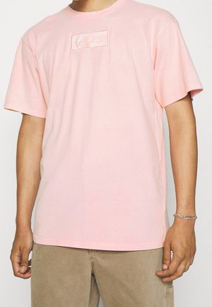 Jasnoróżowa bawełniana koszulka z okrągłym dekoltem. Zawiera prostokątną haftowaną naszywkę na środku. Krótkie rękawy i luźny krój.