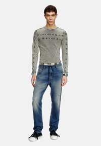 Haut à manches longues gris avec des détails de rayures horizontales, associé à un jean en denim bleu clair avec des accents déchirés et une coupe décontractée.