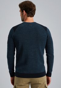 Strickpullover mit Rundhalsausschnitt in Dunkelblau, strukturiertem Körper, kontrastierenden dunklen Schultern, gerippten Bündchen und Saum. Verfügt über ein dekoratives Patch.