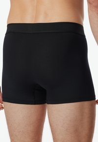 Svarta boxershorts gjorda av ett glatt tyg, med ett elastiskt midjeband och en figurnära passform. Inga synliga logotyper eller mönster.