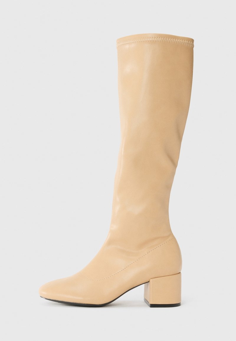 Botte haute en cuir beige avec un bout rond et un talon carré, présentée en vue latérale sur un fond gris clair uni.