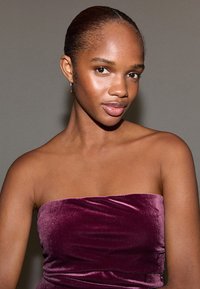 Bordo sametový top bez ramínek s hladkou texturou. Subjekt má uhlazené vlasy a jednoduché náušnice, pózuje před neutrálním pozadím.