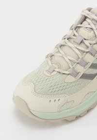 Chaussure de course légère en vert menthe et beige. Tige en mesh avec des accents texturés et des détails réfléchissants. Semelle en caoutchouc robuste avec un motif de traction.