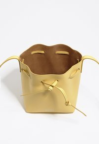 Gelbe Leder-Eimer-Tasche mit gewelltem oberen Rand, Kordelzugverschluss und glattem Innenraum. Logo auf der Vorderseite aufgedruckt.