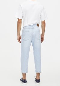 Ljusblå denimjeans med avslappnad passform, uppvikta benslut och en brun läderlapp. Har två bakfickor och lätt slitningar.