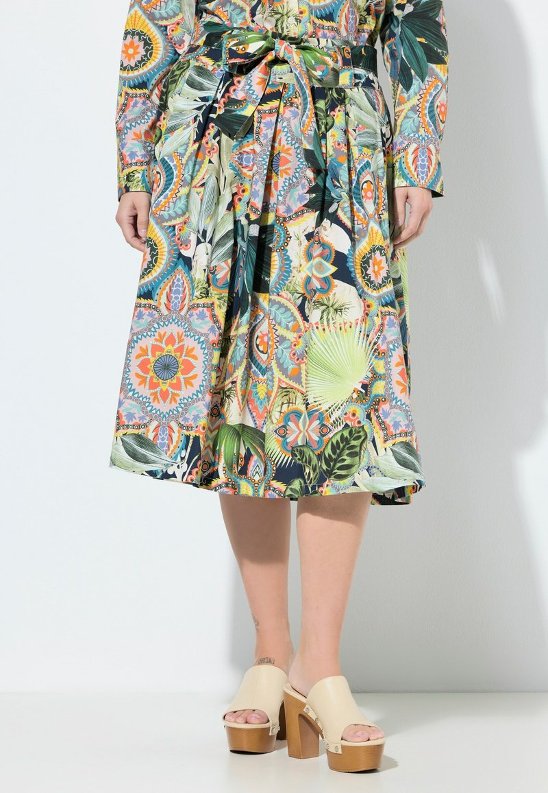 Midirock mit bunten Blumen- und geometrischen Mustern, gebundener Gürtel in der Taille, kombiniert mit cremefarbenen Plateau-Open-toe-Absätzen.