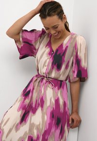 Mikadress med ett flerfärgat mönster i rosa, beige och svart. Den har en V-ringning, knäppning framtill och ett bälte i midjan med utställda ärmar.