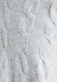 Pull en tricot gris clair avec un motif en câble texturé. La surface semble douce et duveteuse, avec des motifs surélevés de manière uniforme.