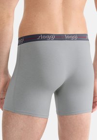 Grå boxershorts tillverkade av mjukt material med en åtsittande passform. Har ett mörkt midjeband med varumärket "sloggi" och en röd accentlinje.