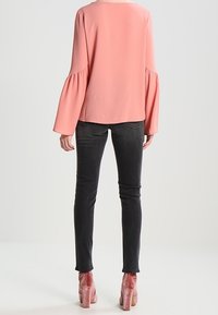 Blouse rose à manches évasées en tissu léger, associée à un jean skinny noir et des chaussures à talons blocs en suède rose.