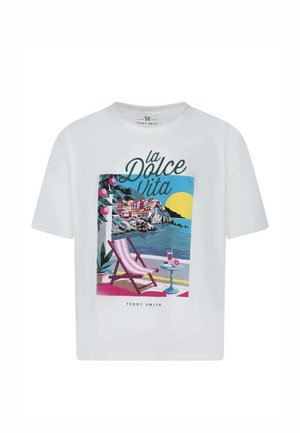 T-shirt blanc avec illustration colorée de bord de mer, fauteuil à rayures roses, table avec boisson, village côtier, soleil et texte "La Dolce Vita".