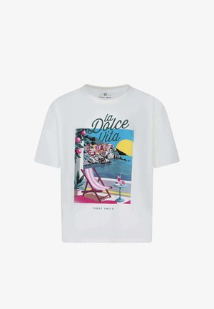 T-shirt blanc avec illustration colorée de bord de mer, fauteuil à rayures roses, table avec boisson, village côtier, soleil et texte "La Dolce Vita".