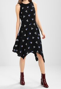 Vestido negro sin mangas con un dobladillo acampanado, que presenta patrones florales en azul, rosa y blanco, combinado con botas de tobillo burdeos.