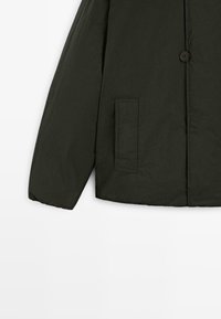 Giacca leggera verde scuro con chiusura a bottoni, una tasca frontale e un tessuto liscio, leggermente strutturato.