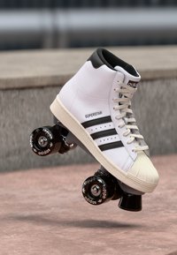 Λευκό ψηλό πατίνι roller skate; δερμάτινο επάνω μέρος με τρεις μαύρες ρίγες; μαύρη τακούνι; καουτσούκ σόλα; στολισμένο με το λογότυπο της Adidas στους τροχούς.