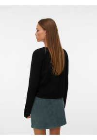 Svart tröja med lång ärm i en enkel design, kombinerad med en grön mocka mini kjol. Minimal detaljer och mjuk textur.